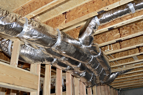 A basement ceiling in a new construction showing the heat/air duct work attached to the framework with PVC pipes in the background.