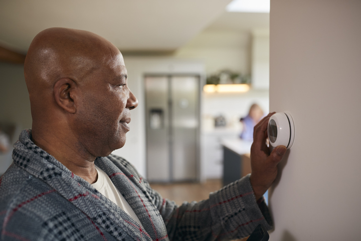 Mature Man Turning Control Dial On Digital Central Heating Thermostat At Home