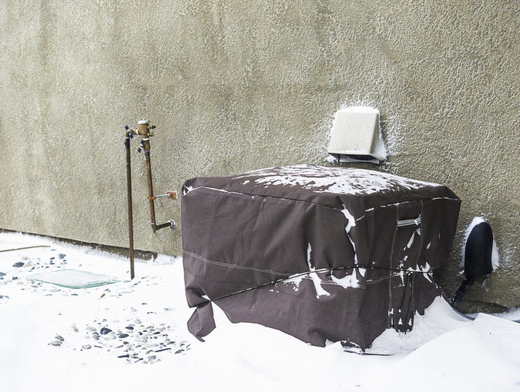 Residential air conditioning unit wrapped with protective cover in blizzard