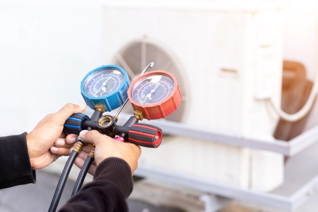 Air repair mechanic using measuring equipment for filling industrial factory air conditioners and checking maintenance outdoor air compressor unit.